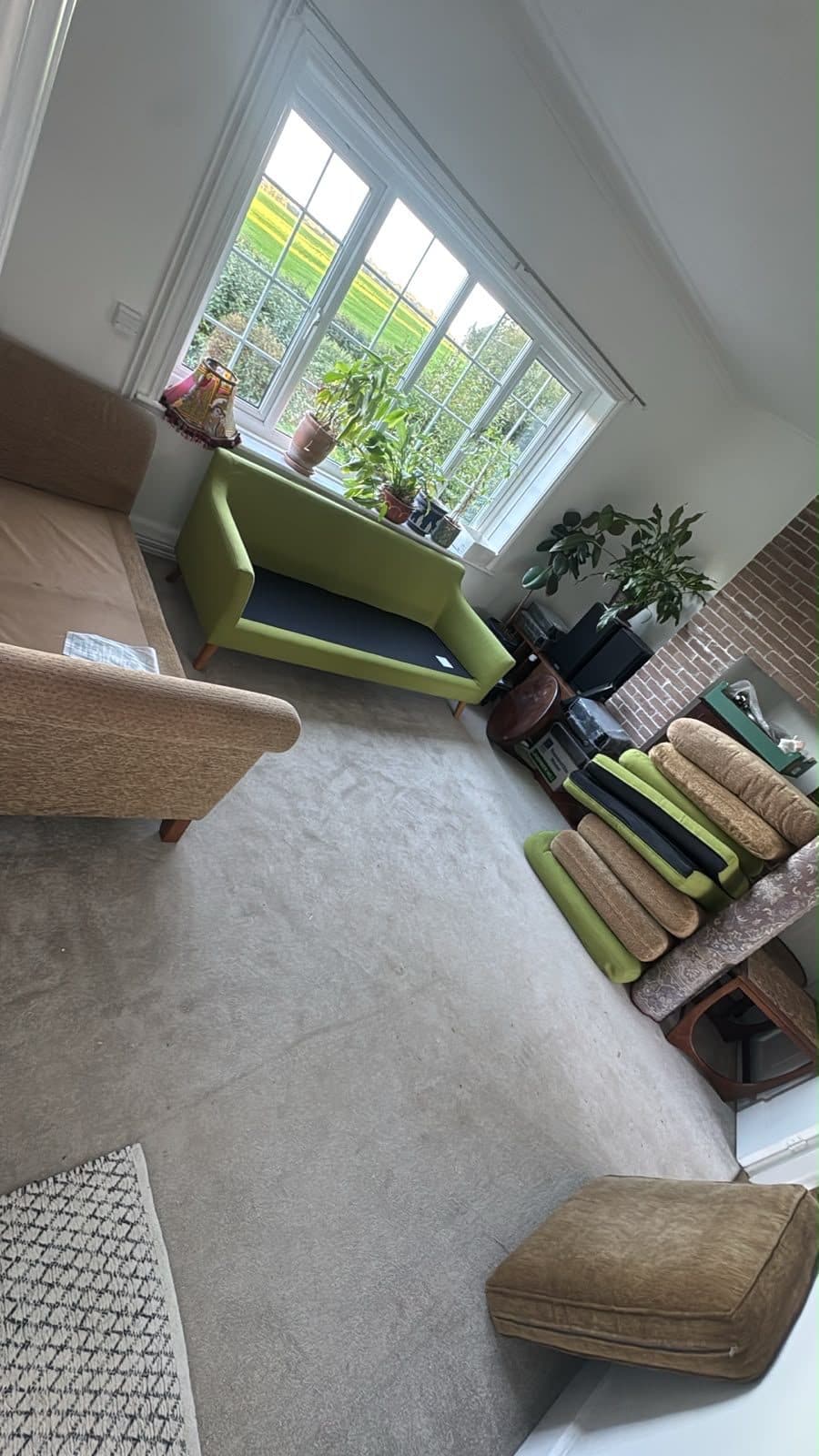 Living room cleared ready to load — sofa, armchair and stacked cushions by the window