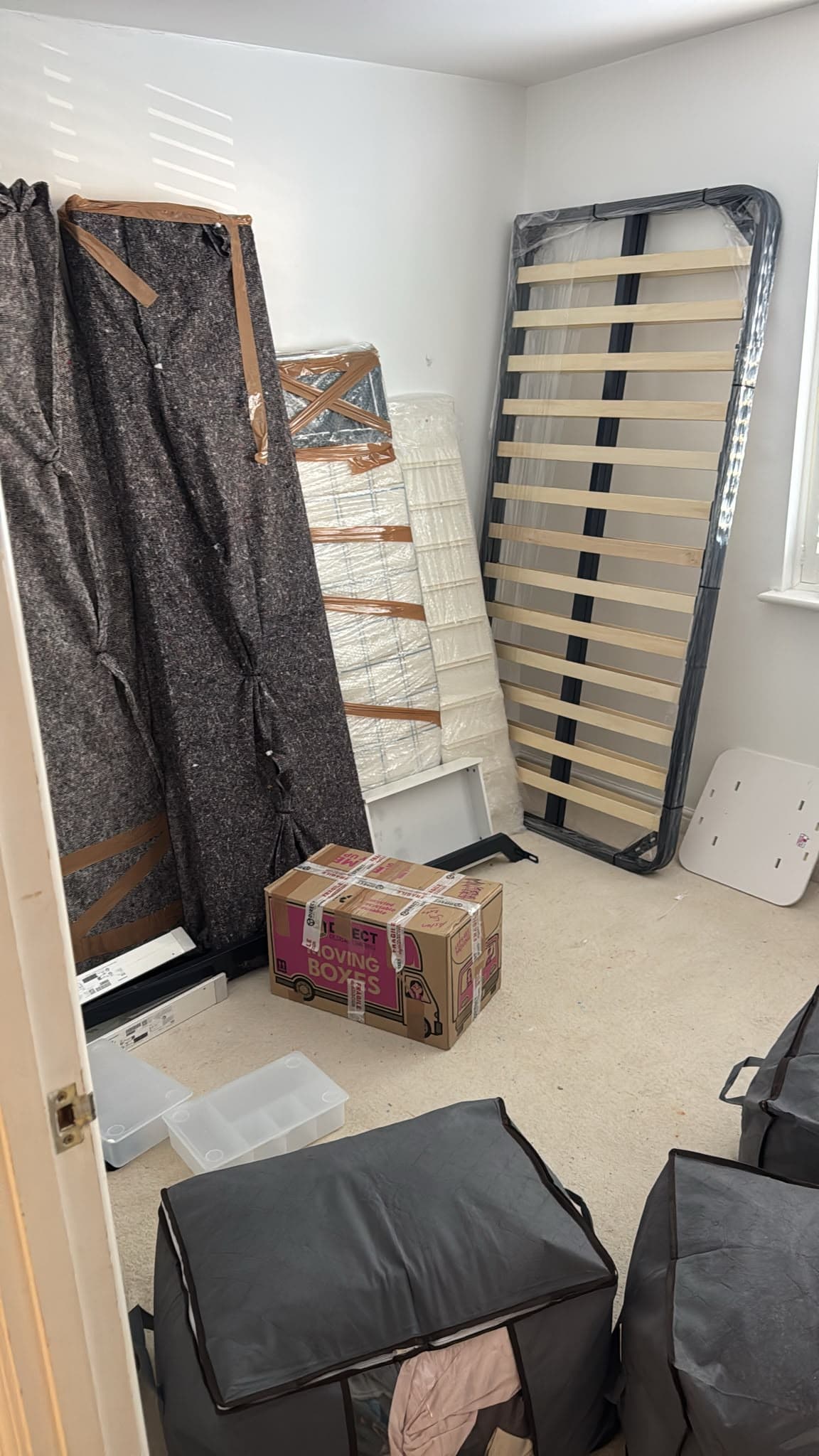 Dismantled bed frame, wrapped mattress and blanket-protected headboard staged for loading