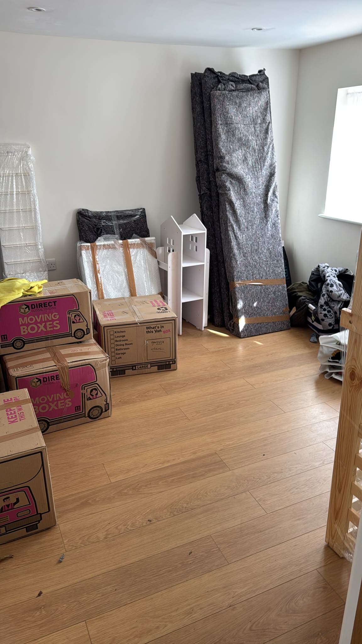 Labelled moving boxes and wrapped furniture staged in a bedroom before collection