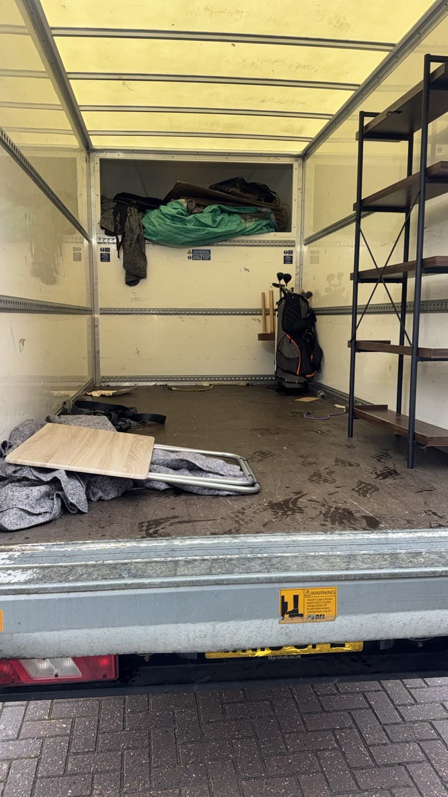 Part-unloaded Luton van showing shelving, a table top and protective blankets partway through the move
